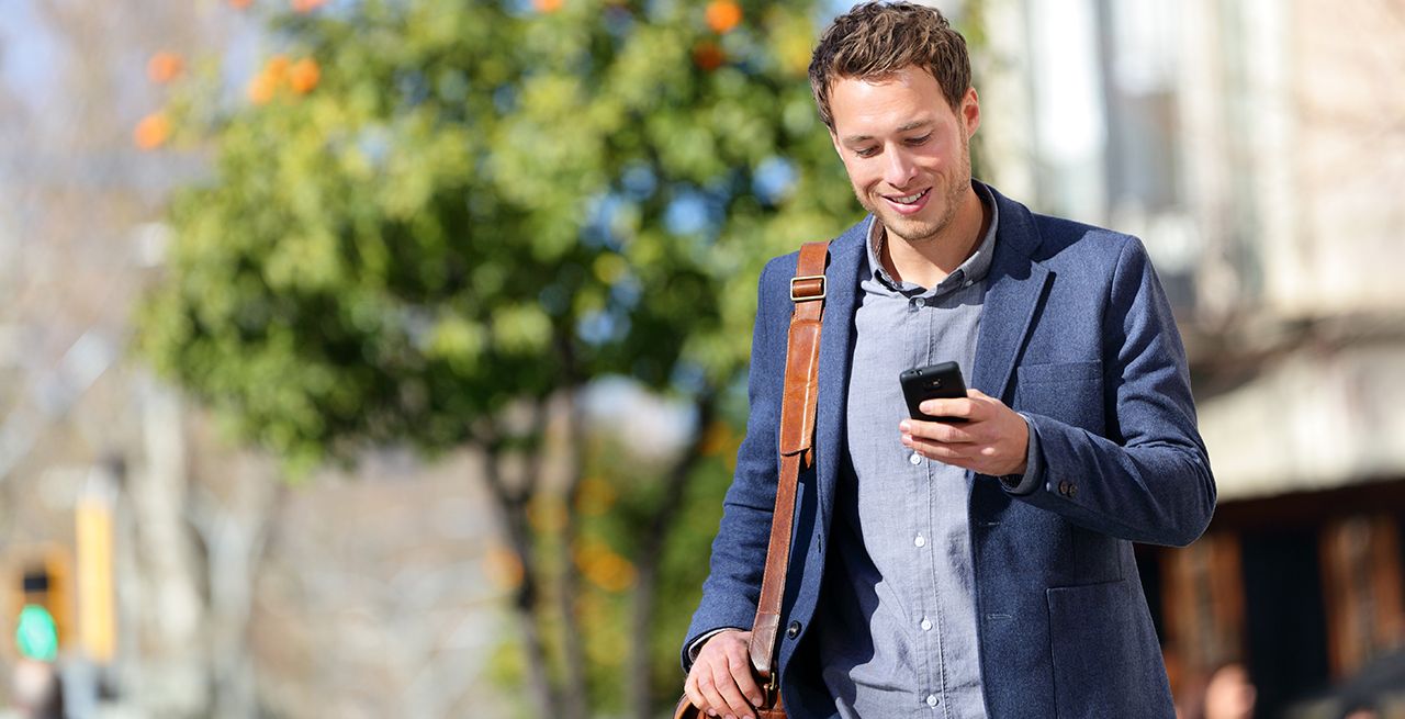 Man walking outside smiling looking at his mobile phone