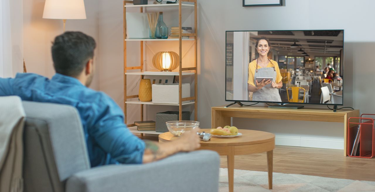 Man watching TV ad in his living room, viewed from behind