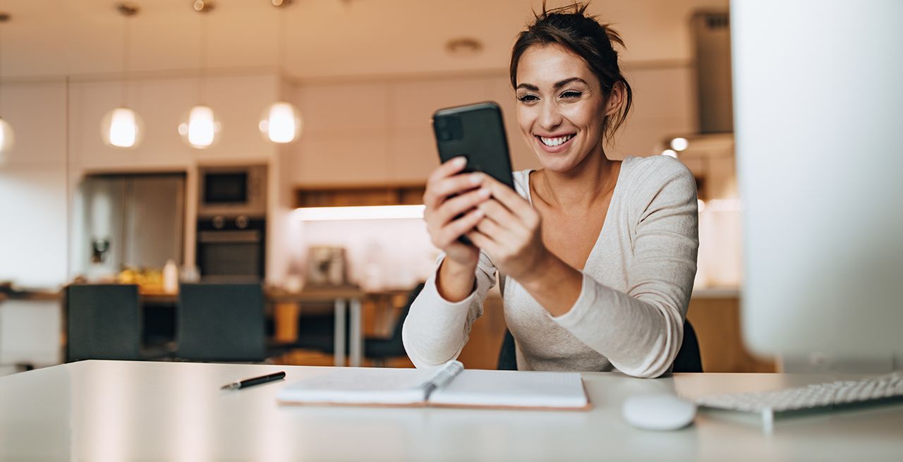 Woman using her cell phone in her kitchen, smiling