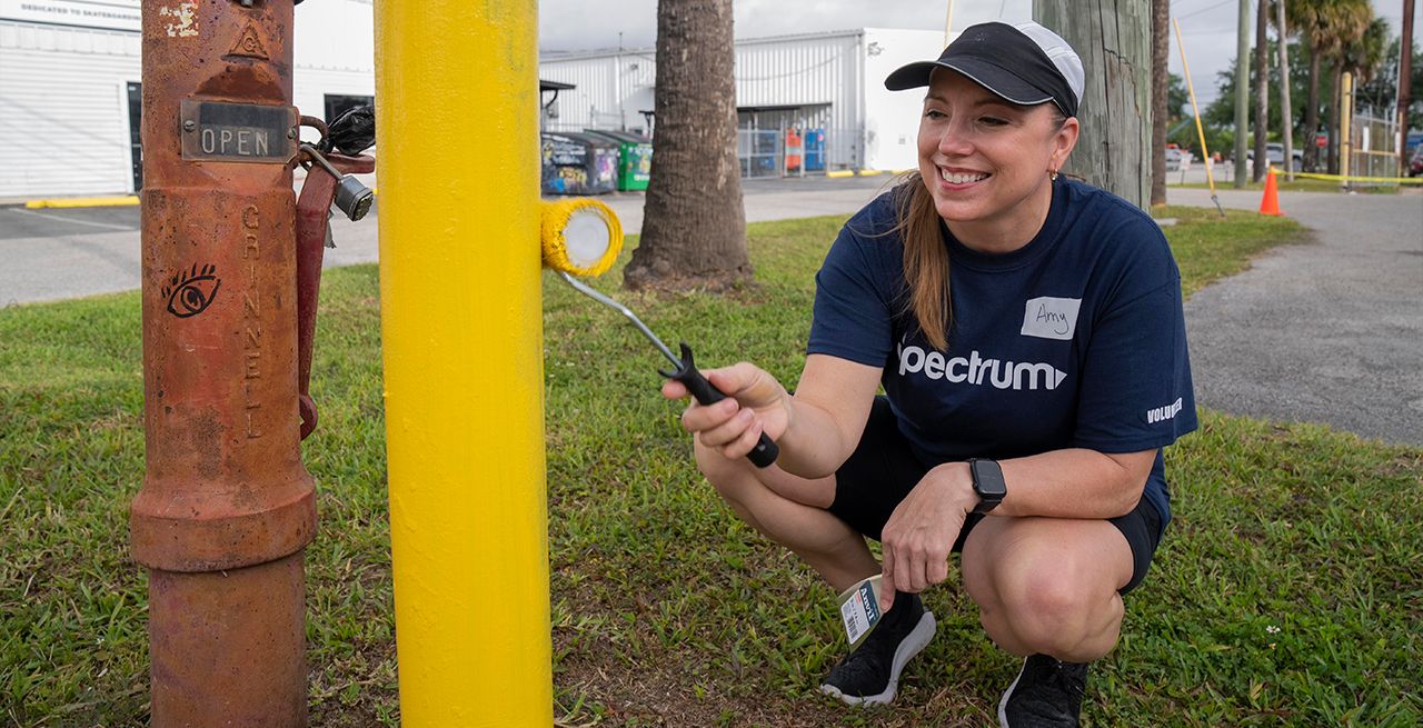 Spectrum Community Center Assist volunteer painting a pole yellow with a roller